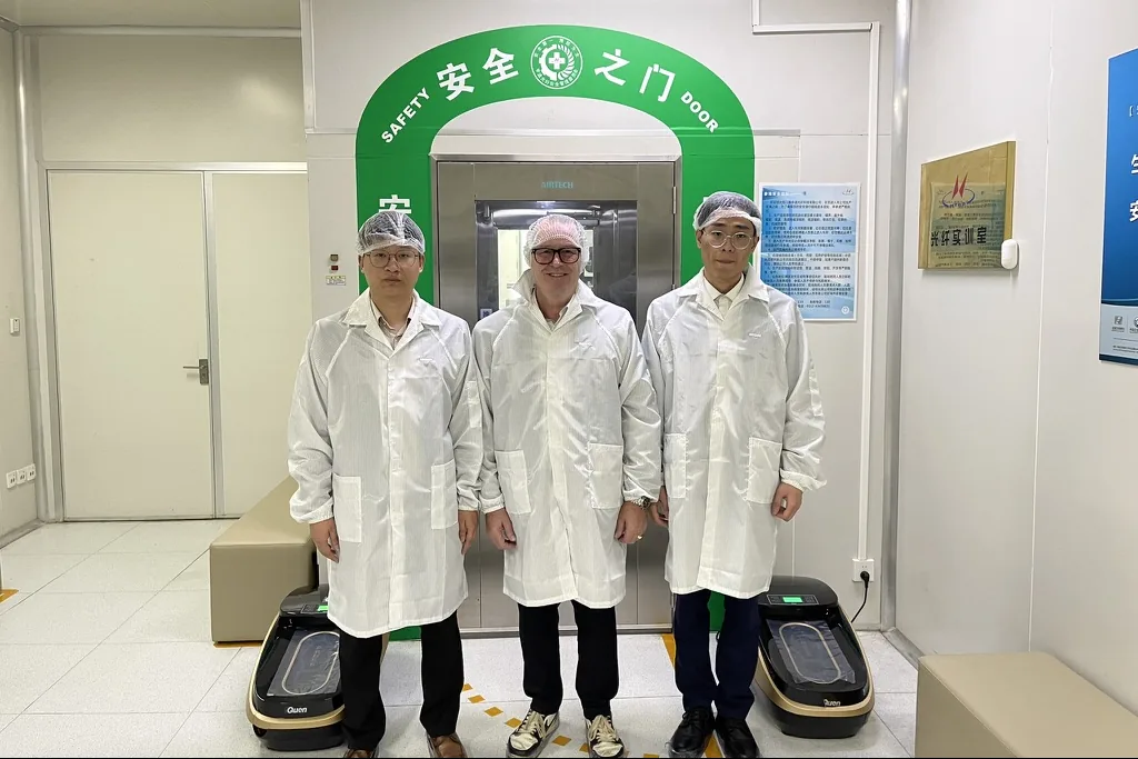 Volker Honsowitz in Schutzkleidung mit zwei Mitarbeitern von Hengtong Optic-Electric vor der Schleuse zum Reinraum